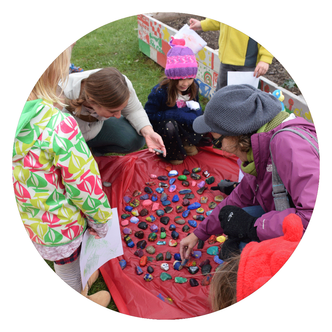 Group of children looking at painted rocks outdoors.