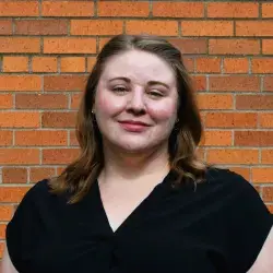 Photo of a smiling white woman with posing in front of a brick wall