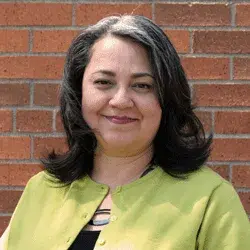 Smiling woman in a green cardigan in front of a brick wall