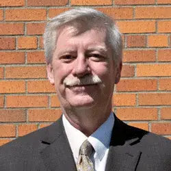 Photo of a smiling white man posing in front of a brick wall