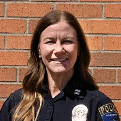 Photo of a smiling white woman wearing a Rochester police uniform posing in front of a brick wall
