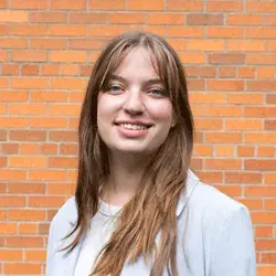 Photo of a smiling white woman posing in front of a brick wall